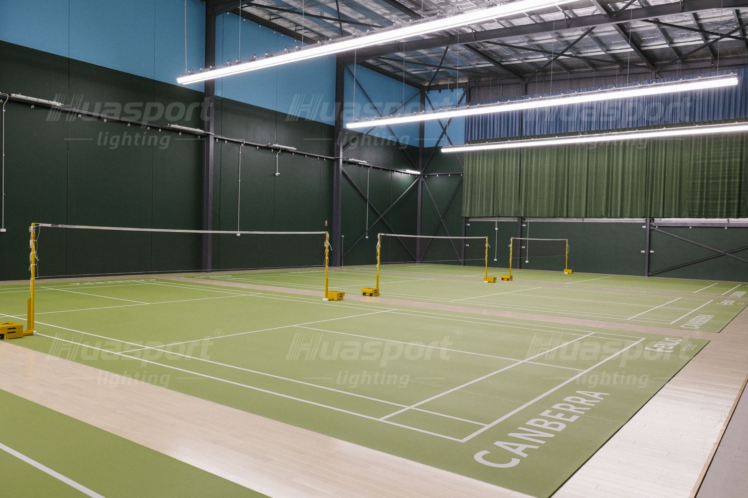 Australian badminton court with yellow net posts and a long-bar fixture row mounted on the side structure