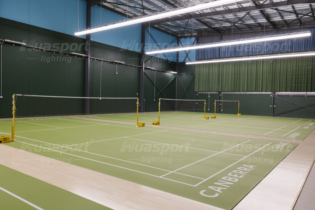 Australian badminton hall with long-bar fixture rows carried above the courts