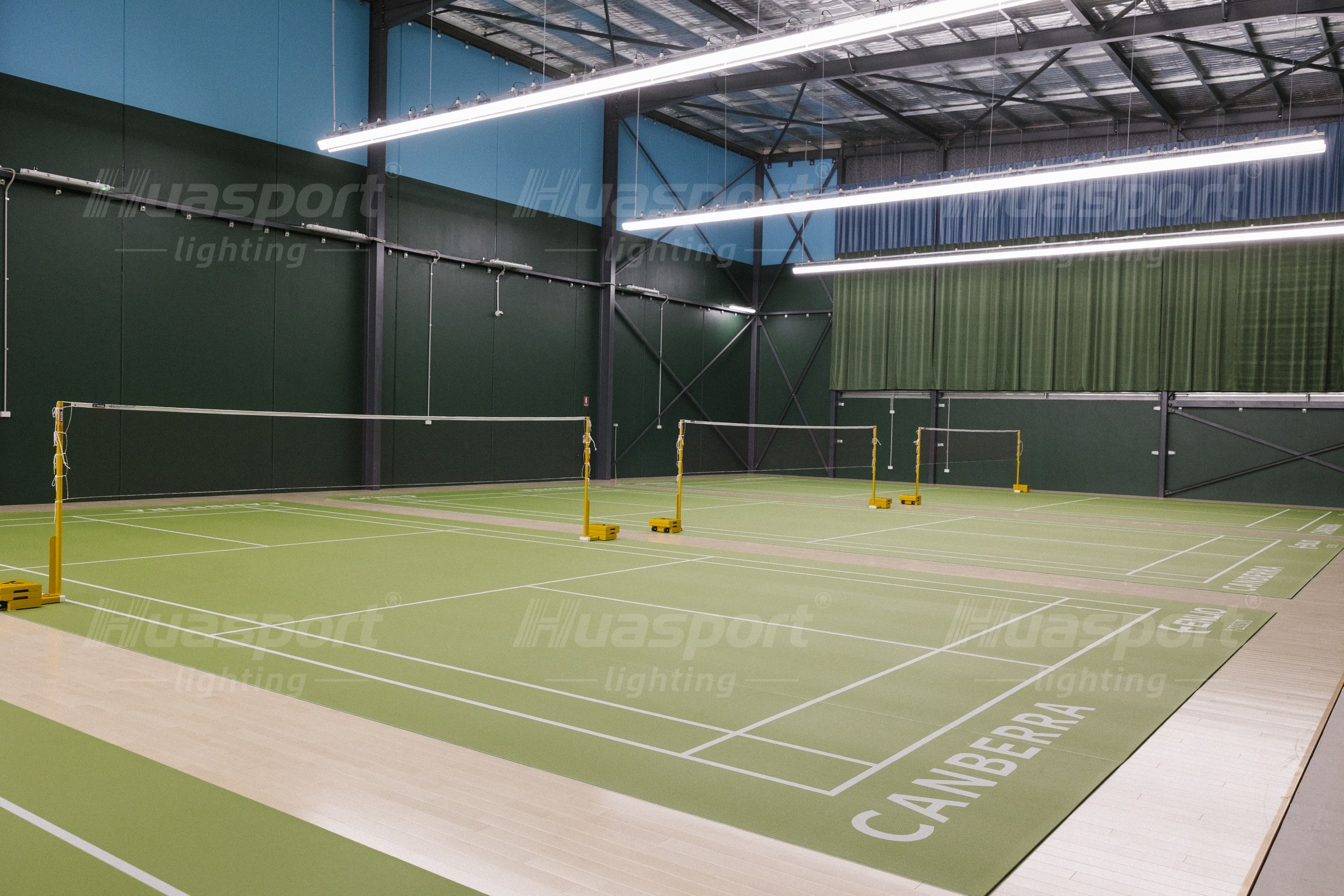 Australian badminton hall with long-bar fixture rows carried above the courts
