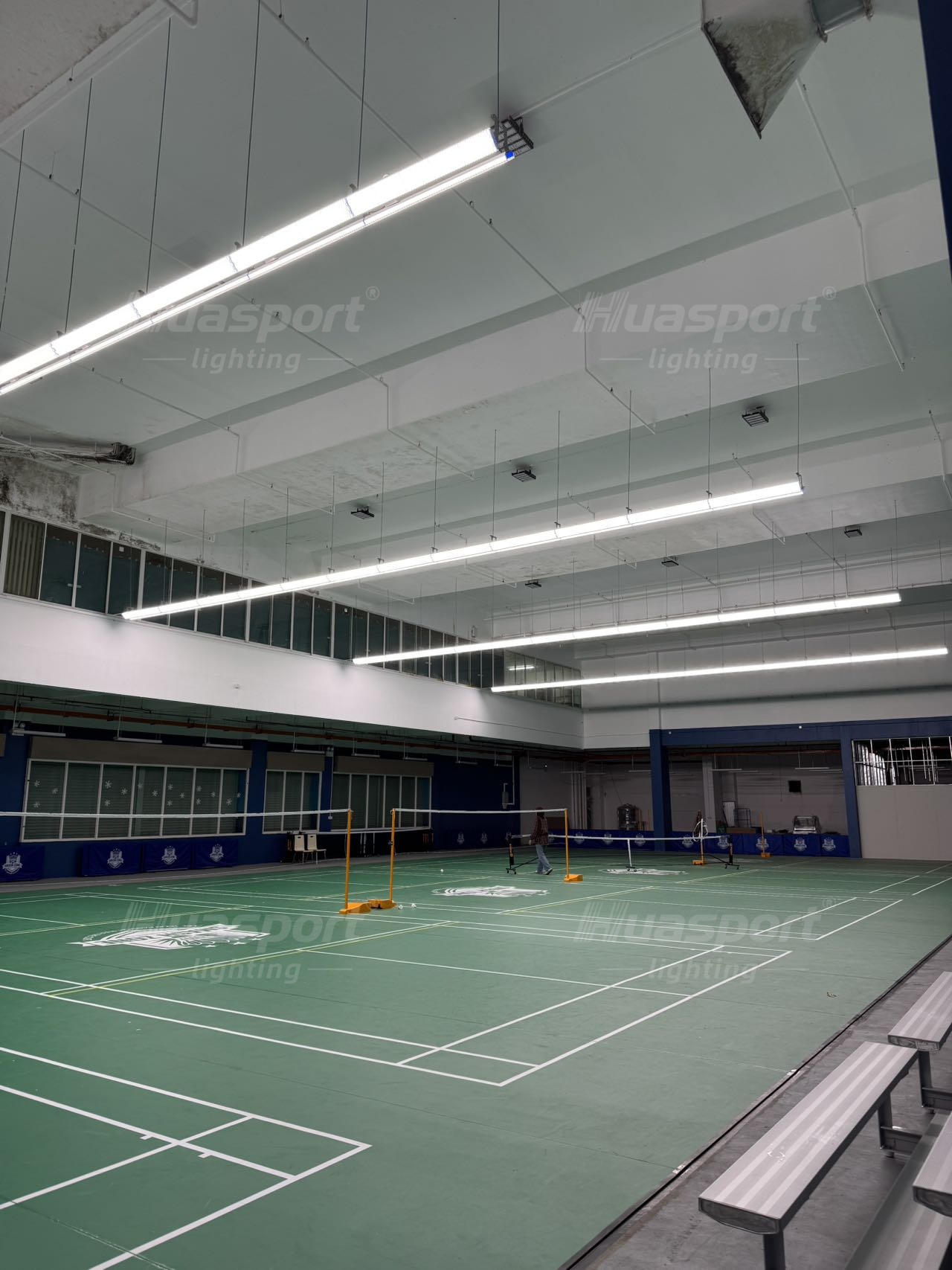 Brunei badminton court lighting row view with long-bar fixtures above green courts