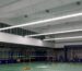 Long-bar lighting rows above a green indoor badminton court in Brunei