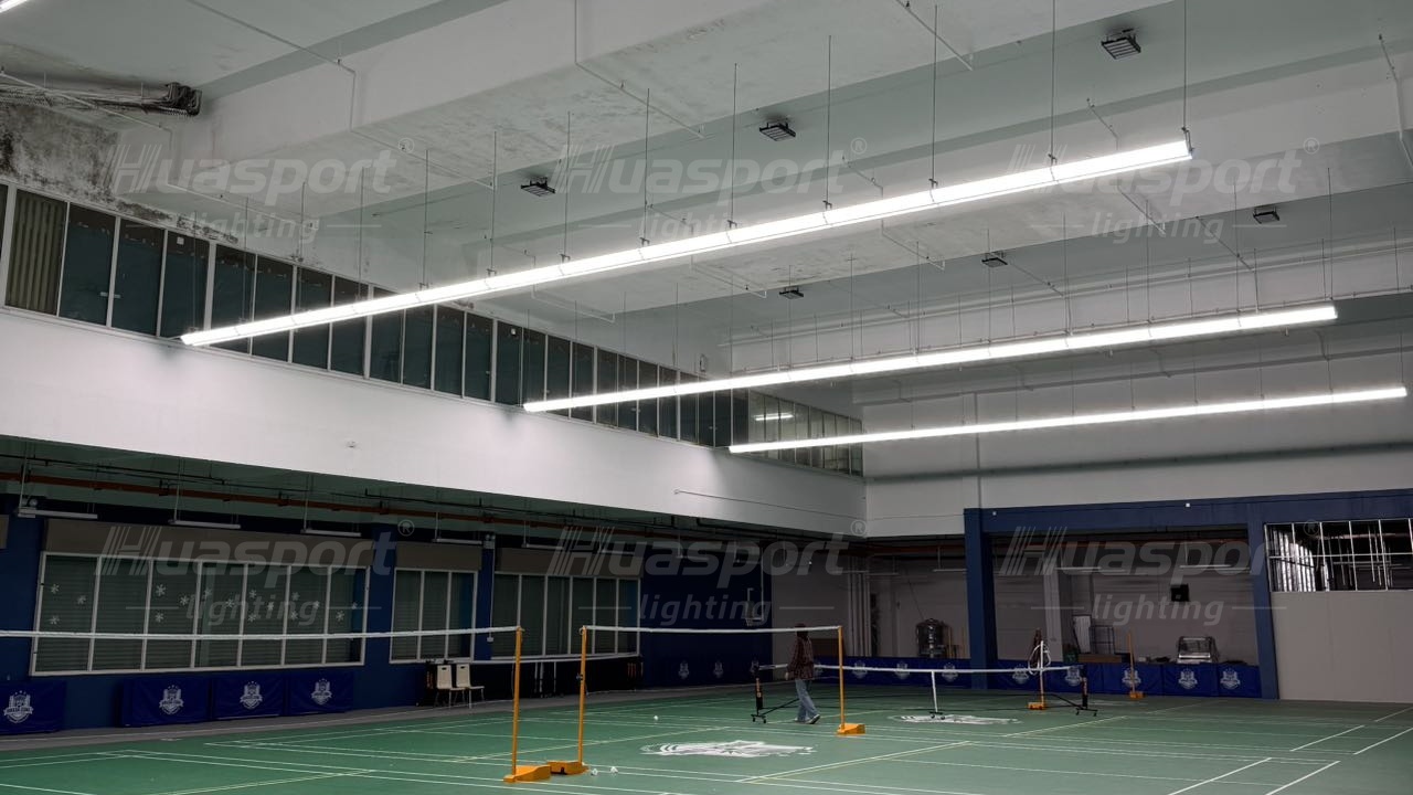 Long-bar lighting rows above a green indoor badminton court in Brunei