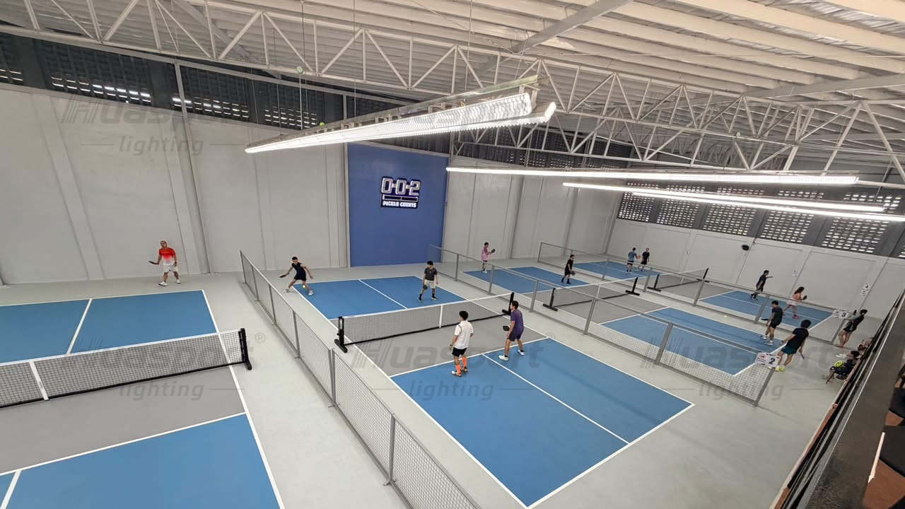 Blue indoor pickleball courts, dividing fences and long-bar ceiling lights in a Philippines venue