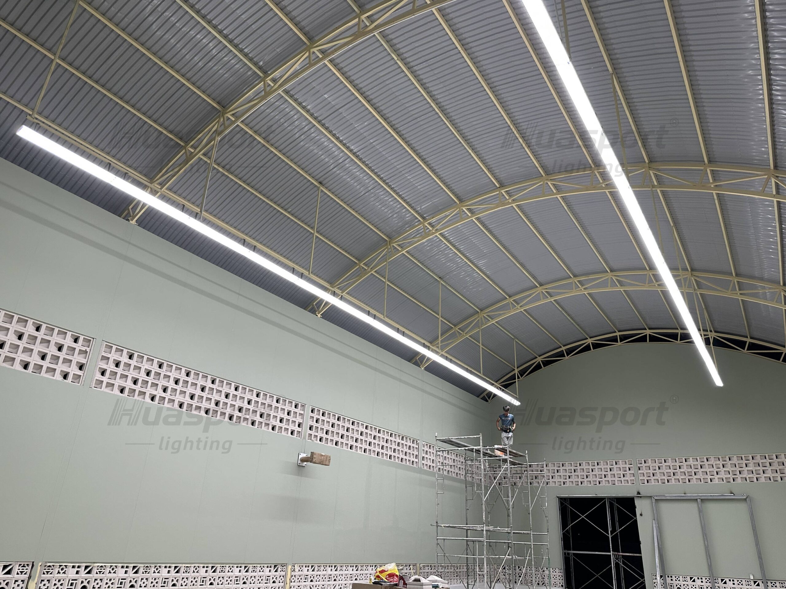 Long-bar lights below yellow roof trusses in a green-walled Vietnam hall during installation